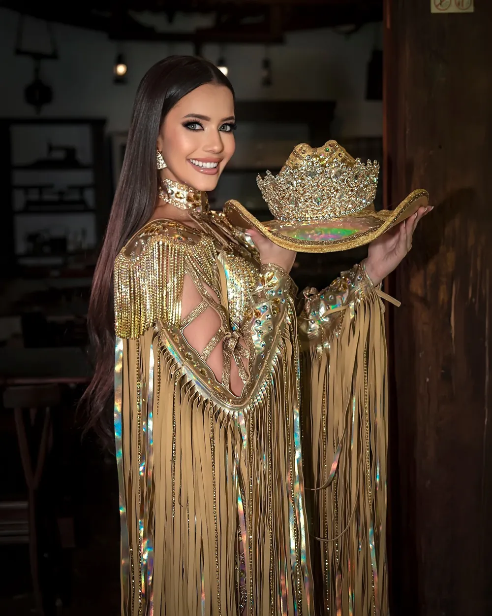 Fabíola Jeanne em traje dourado, segurando o chapéu com a coroa